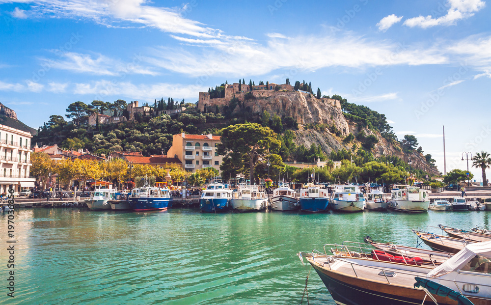 Boats moored in harbour with Chateau de Cassis atop a hill in background on bright sunny day in Cassis, France