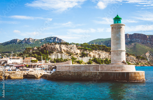 Lighthouse on pier and Chateau de Cassis castle in background on bright sunny day in old port of Cassis, France