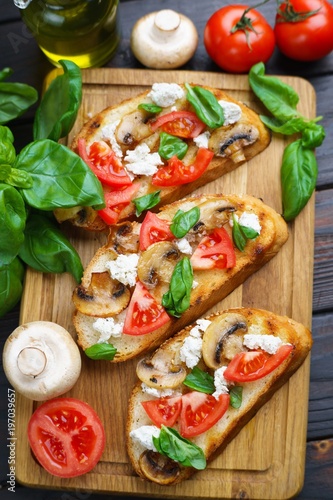 Tasty homemade Italian antipasti bruschetta with chopped tomatoes, champignons, ricotta and basil on grilled baguette, view from above