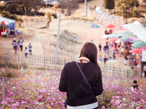 summer travel concept from front side of asian woman traveler and photographer with long black hair during see view and prepare to take photo to flower field with sunny and soft focus background photo