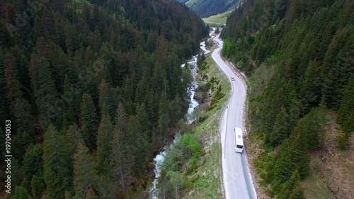 Aerial view of driving white color bus by a road in a mountainous area between the pine forest in Austria.