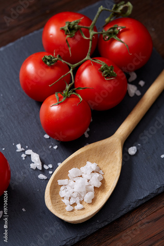 Vegetarian still life with fresh grape tomatoes, pepper and salt in wooden spoon on wooden background, selective focus