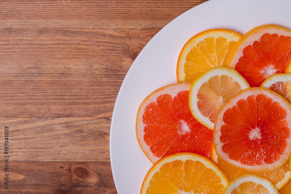 orange grapefruit and lemon cutting into a plate on a wooden background orange grapefruit and lemon cutting into a plate on a wooden background