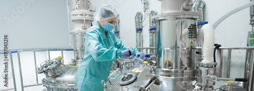 Pharmaceutical factory woman worker in protective clothing operating production line in sterile environment photo