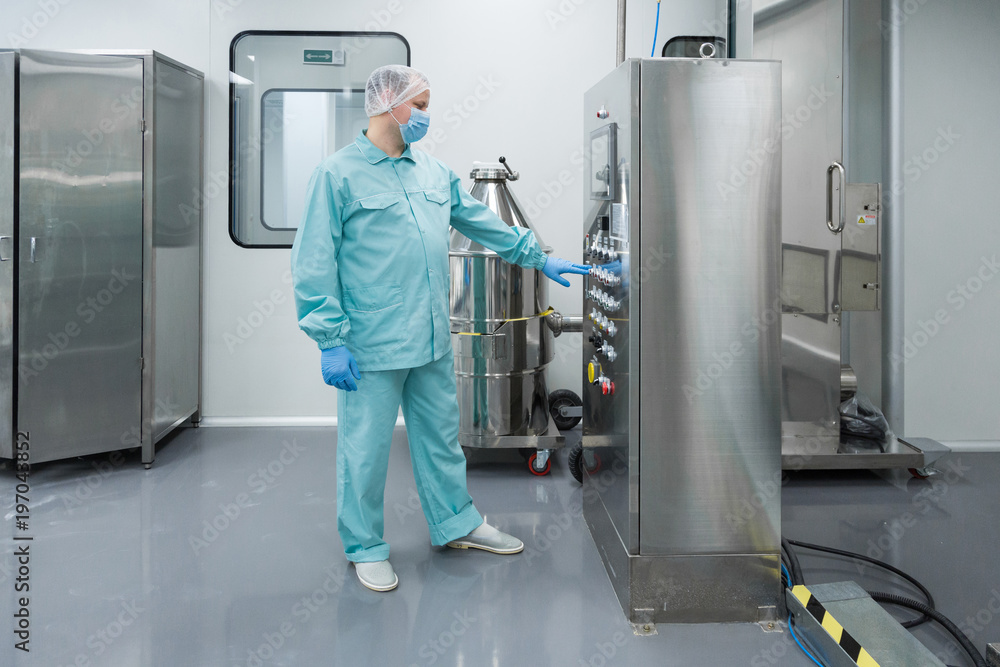 Pharmaceutical factory man worker in protective clothing working with control panel in sterile working conditions Pharmaceutical factory man worker in protective clothing working with control panel in sterile working conditions