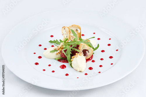 Delicious dessert. Three pieces of ice cream with strawberry and green leaves of arugula, and thin rusks in the centre of a white plate with dots of strawberry jam.
