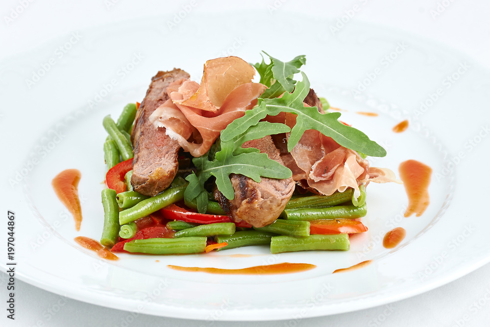 Delicious meal. Grilled beef with pork slices and boiled pepper, green beans, fresh arugula and sauce on a white plate.