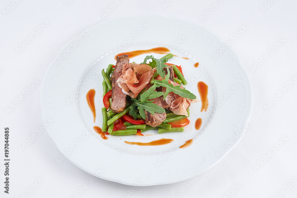 Delicious meal. Grilled tasty beef with pork slices and boiled pepper, green beans, fresh arugula and sauce on a white plate.