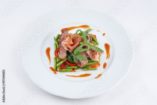 Delicious meal. Grilled tasty beef with pork slices and boiled pepper, green beans, fresh arugula and sauce on a white plate.