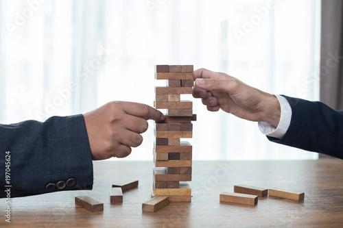 Two Businessman hands play wood block tower game.