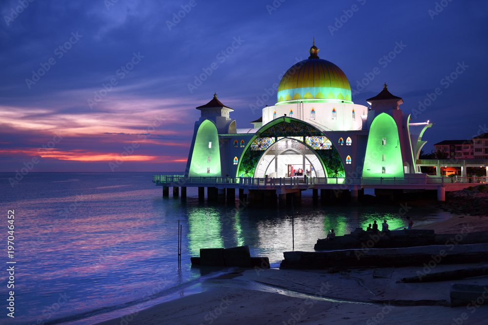 Glowing Strait Mosque of Malacca during sunset and blue hour. The so called swimming Mosque is located at the Historical Malacca City, Malaysia.