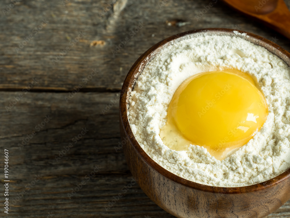 Wooden bowl with flour and broken chicken egg on rustic background Wooden bowl with flour and broken chicken egg on rustic background
