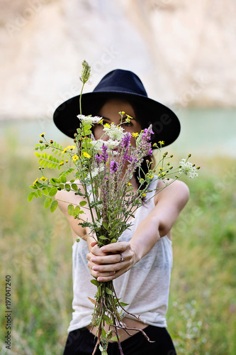 Giovane donna sorridente all'aperto nella natura nascosta da un bouquet di fiori di campo 