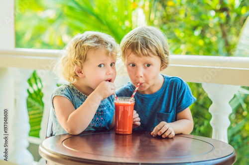 Children boy and girl drink orange smoothie from papaya photo