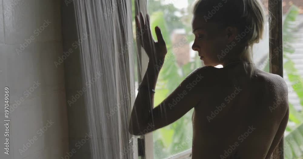 awesome nice topless young girl or woman in shape looking out the window in the bathroom, water flowing from the shower, she is trying it Stock-video | Adobe Stock