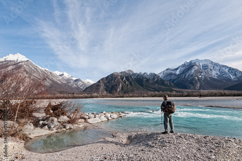 Man hiker on shore of river looking the mountains.