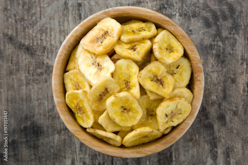 Banana chips in bowl on wooden table. Top view