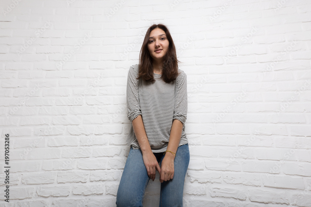 A young pretty smiling girl against a white loft-style brick wall. She looks at the viewer. Copy space. A young pretty smiling girl against a white loft-style brick wall. She looks at the viewer. Copy space.