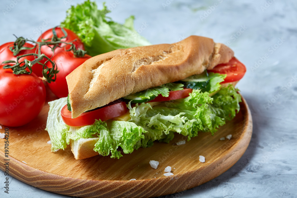 Obraz premium Fresh sandwich with lettuce, tomatoes and cheese served on wooden plate over white textured background, selective focus