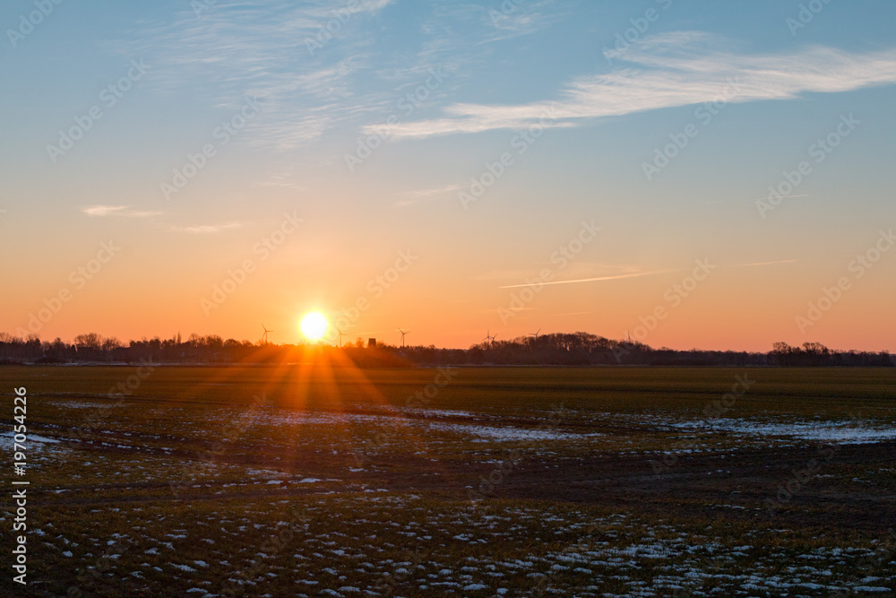 sonnenaufgang oder sonnenuntergang über einem landwirtschaftlichem Feld mit Schnee und Windrädern