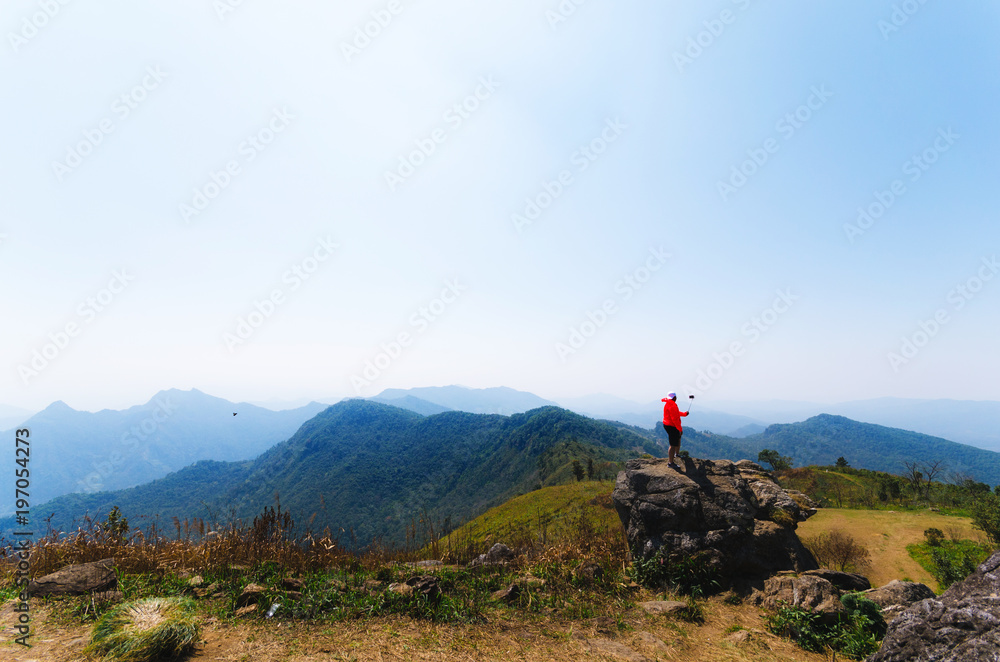 someone in orange jacket stand on a big rock on peak mountain natural landscape with blue sky on the vacation day.