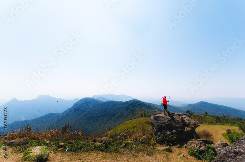 someone in orange jacket stand on a big rock on peak mountain natural landscape with blue sky on the vacation day. © thithawat