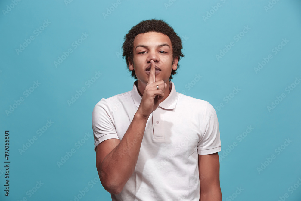 The young man whispering a secret behind her hand over blue background The young man whispering a secret behind her hand over blue background