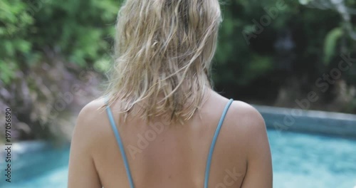 young beautiful blond girl or woman getting ready to swim, taking off her shirt, wearing bikini. summer vacation mood, swimming pool nearby