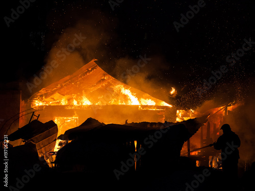 Firefighter at burning fire flame on wooden house roof