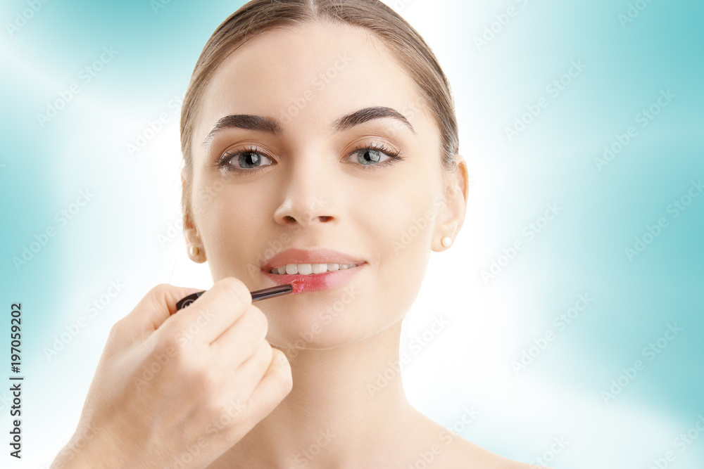 Young woman applying lipstick against blue isolated background Young woman applying lipstick against blue isolated background