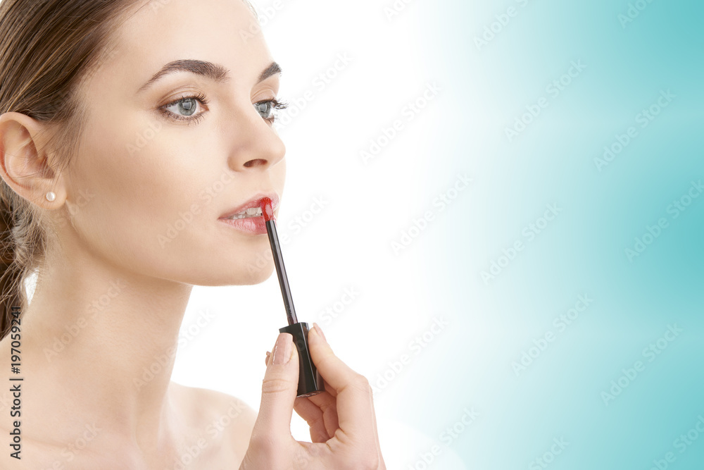 Young woman applying lipstick against blue isolated background