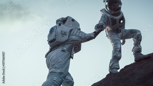 Tableau sur toile Two Astronauts Climbing Mountain Hill Helping Each Other, Reaching the Top