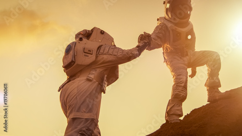 Two Astronauts Climbing Mountain Hill Helping Each Other, Reaching the Top. Helping Hand. Overcoming Difficulties, Important Moment for the Human Race.
