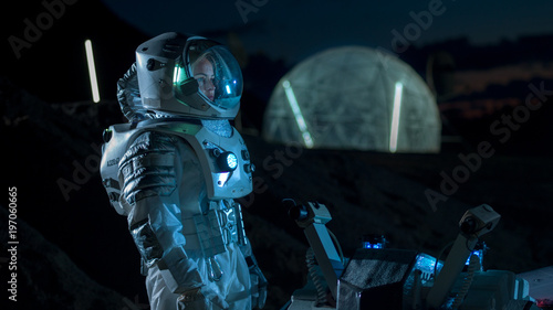 Astronaut Looking Around while Standing near Rover on the Alien Planet at Night. In the Background His Base/ Research Station. Space Exploration, Colonization Theme.