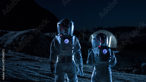 Two Astronauts in Space Suits Walk on the Alien Planet Looking at the Sky. In the Background Base with Geodesic Dome. Other Worlds Colonization and Space Travel Concept.