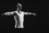Athletic muscular man exercising with elastic expander at black