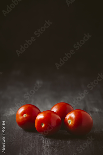 Four tomatoes on a black wooden background.