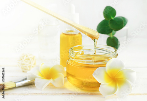 Honey spa treatment. Pouring sweet golden honey to jar, plumeria flowers, soft sunny light. Natural homemade skincare.