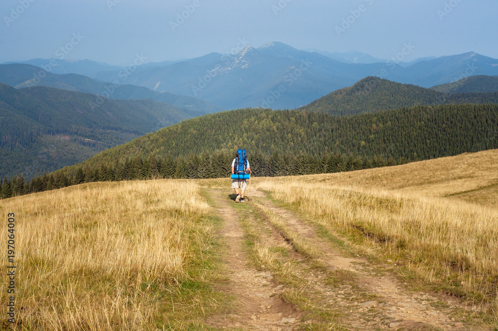 Backpacker walking on the path. Mountain range at the background.