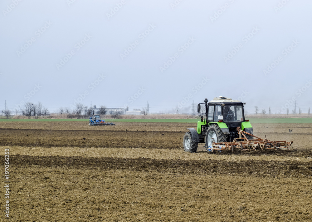 Fototapeta premium Lush and loosen the soil on the field before sowing. The tractor plows a field with a plow