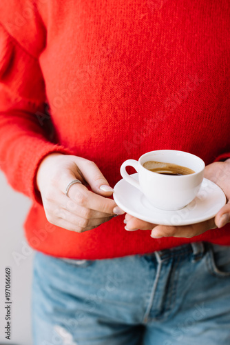 Young woman in a red sweater holding a cup of fresh espresso coffee, cropped photo