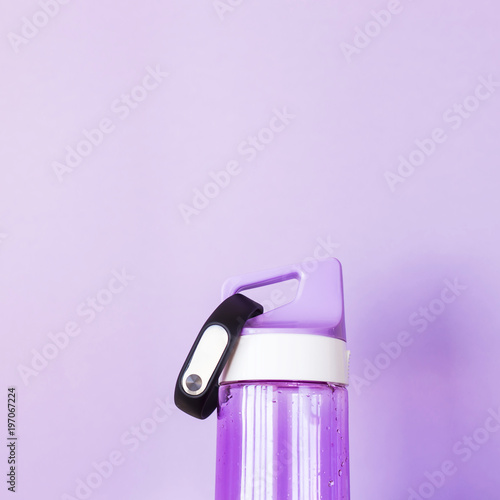 Purple water bottle for sports and fitness bracelet on a bright purple background. Healthy lifestyle and fitness concept. Background  copyspace