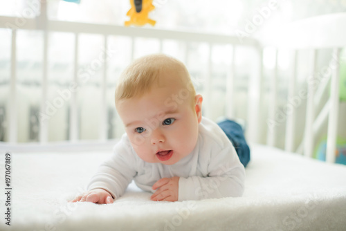 Funny baby in white crib with canopy. Nursery interior and bedding for kids. Laughing little boy playing. Bedroom for young children. Happy child in white pajamas.
