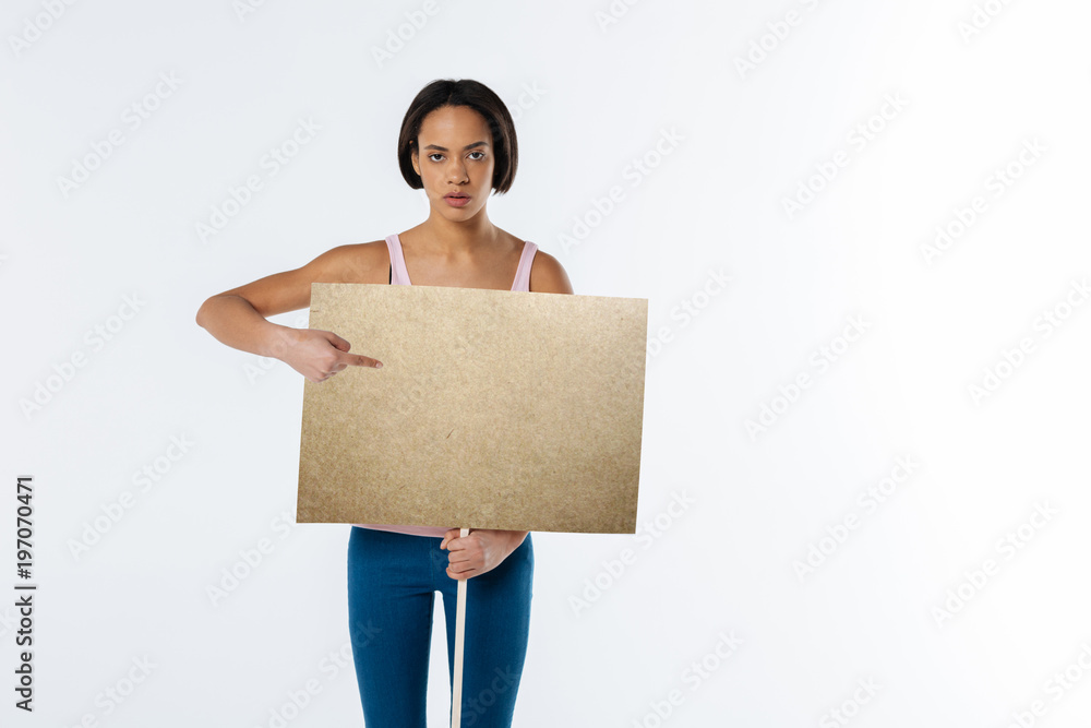 Read it. Serious unhappy young woman holding a sign and pointing at the inscription on it while participating in the protest Read it. Serious unhappy young woman holding a sign and pointing at the inscription on it while participating in the protest