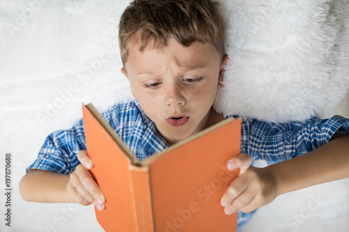 little boy is lying on the bed and reading a book