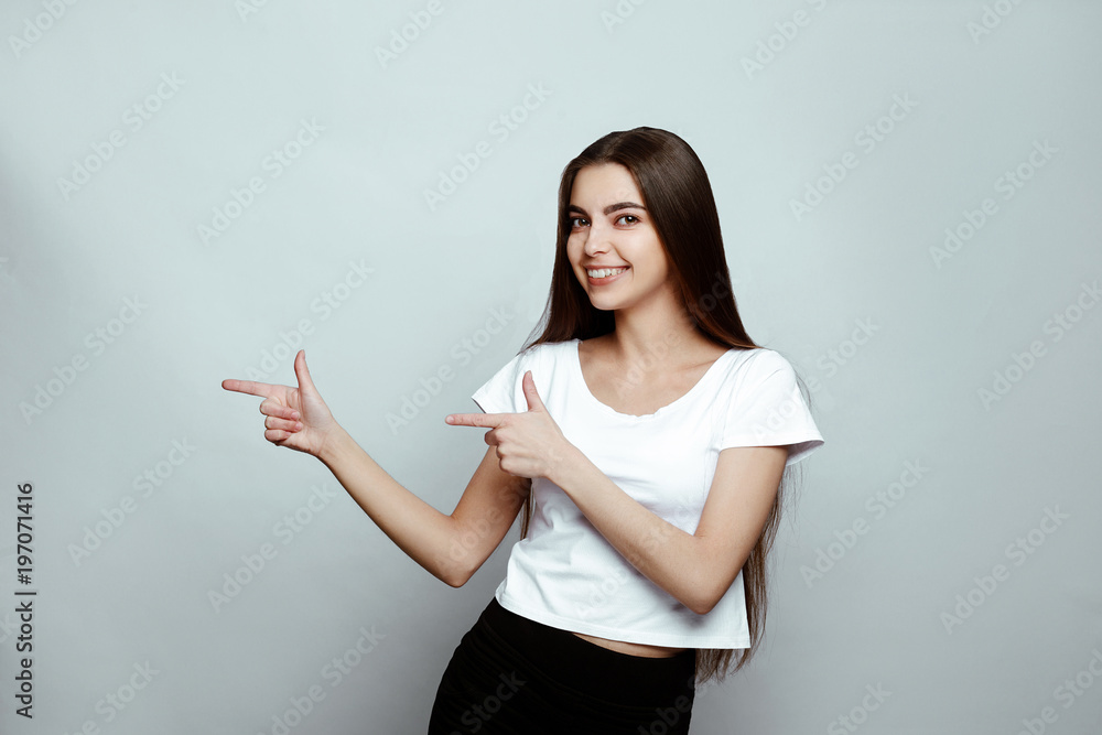 human emotions. Portrait of the young beautiful woman brunette with long dark brilliant hair. The girl poses on a white background, smiling cheerfully and pointing with forefingers away human emotions. Portrait of the young beautiful woman brunette with long dark brilliant hair. The girl poses on a white background, smiling cheerfully and pointing with forefingers away