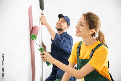 Young decorators painting wall in room