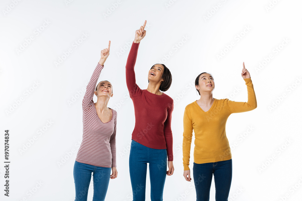 So interesting. Attractive pleasant cheerful women holding their hands and pointing up while seeing interesting things So interesting. Attractive pleasant cheerful women holding their hands and pointing up while seeing interesting things