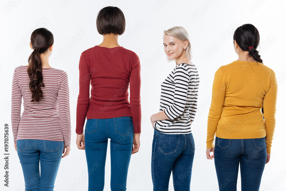 Obraz premium Positive attitude. Joyful nice blonde woman turning to you and smiling while standing among her friends