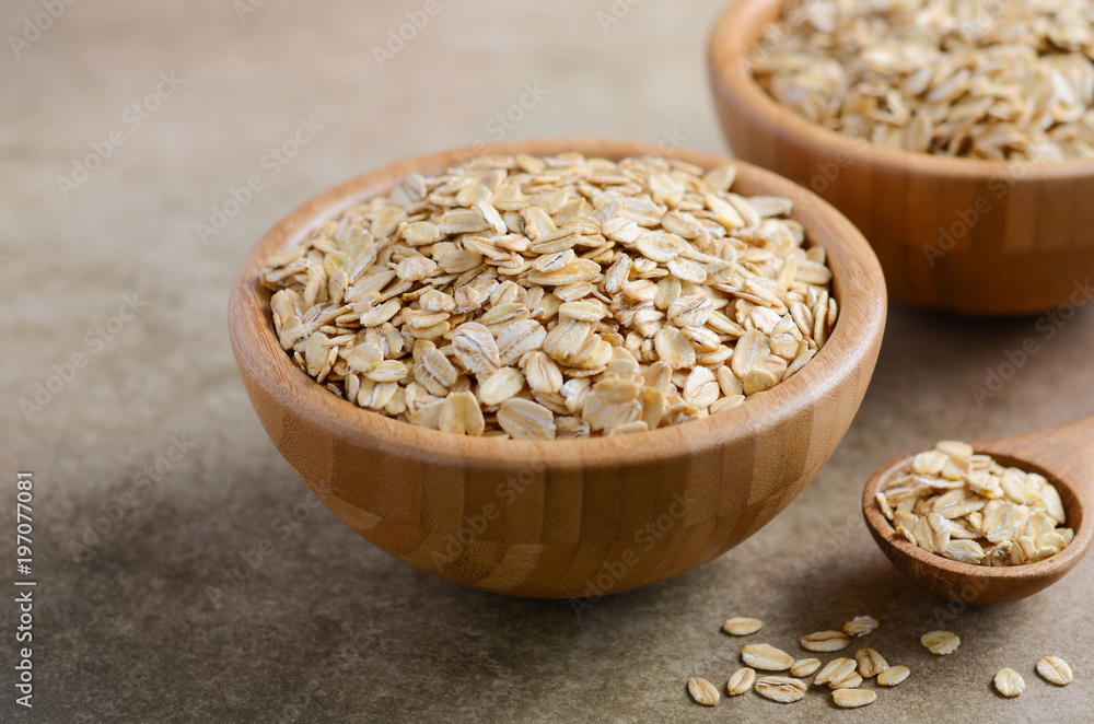 Oat flakes in a wooden bowl and wooden spoon on light brown background, selective focus. Oat flakes in a wooden bowl and wooden spoon on light brown background, selective focus.